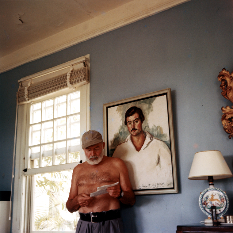 EH-C176T Ernest Hemingway at his home in Cuba, circa 1953, standing in front of a 1929 portrait of himself by Waldo Pierce. Photograph in the Ernest Hemingway Photograph Collection, John F. Kennedy Presidential Library and Museum, Boston.